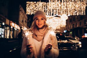 Frau in wolliger Kleidung mit Wunderkerzen unter leuchtender Weihnachtsdeko