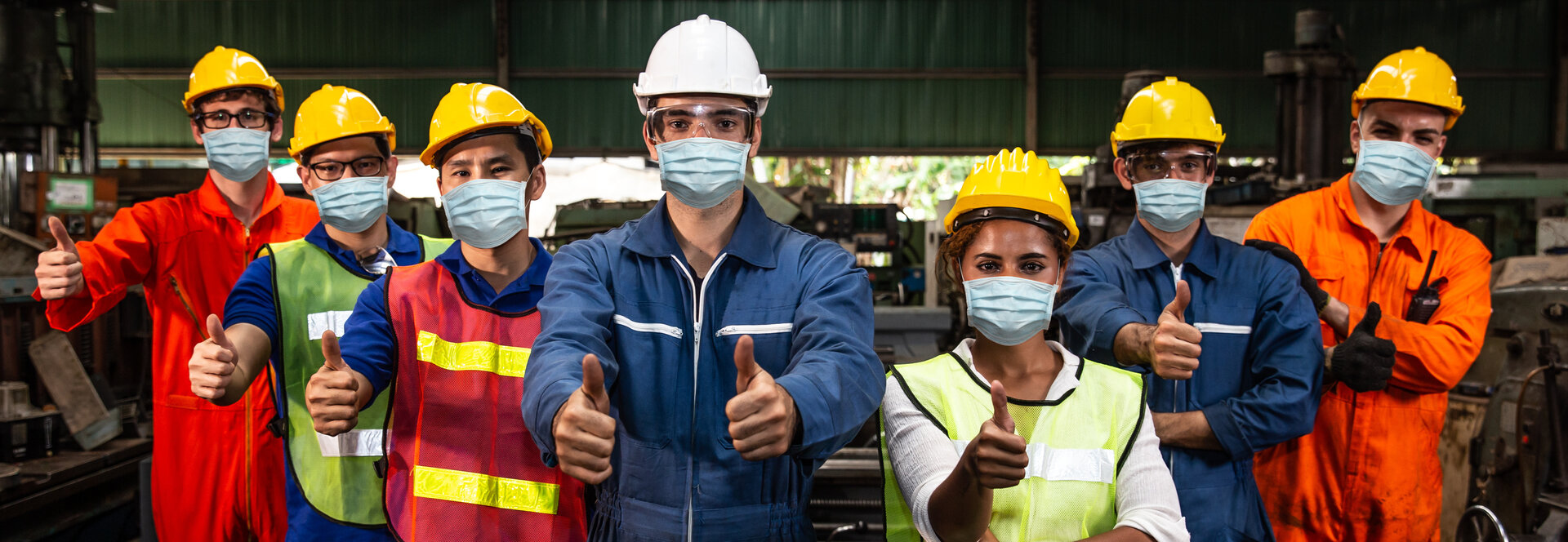 Eine Gruppe von Arbeitern, die Atemschutzmasken gegen Luftstaubverschmutzung tragen, stehen nebeneinander in einer Fabrik