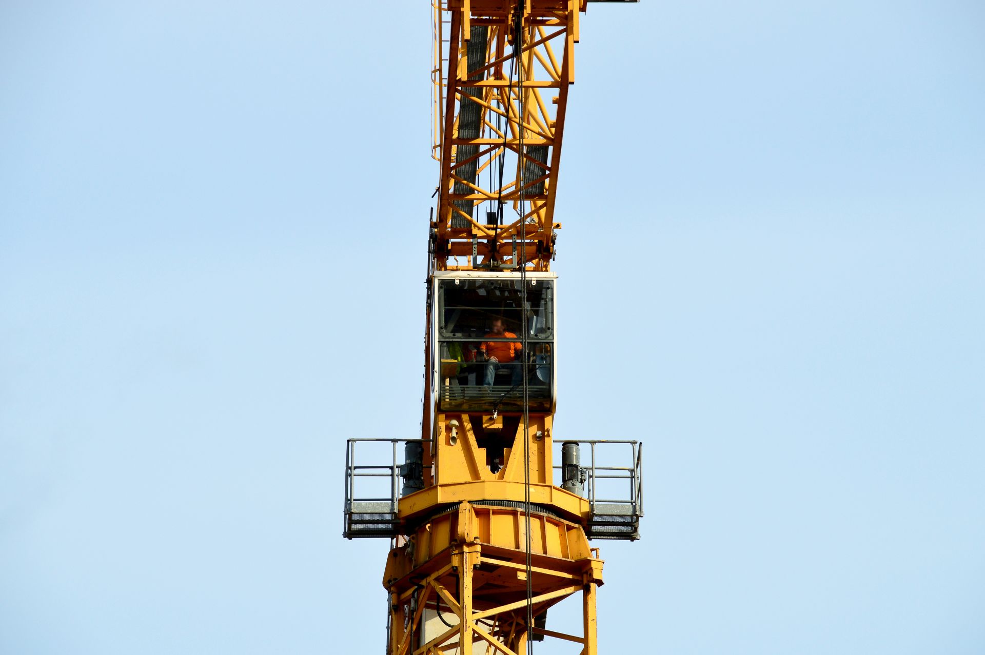 Kranfuehrer sitzt in Kabine eines gelben Turmdrehkrans und blickt auf die Baustelle aus grosser Hoehe